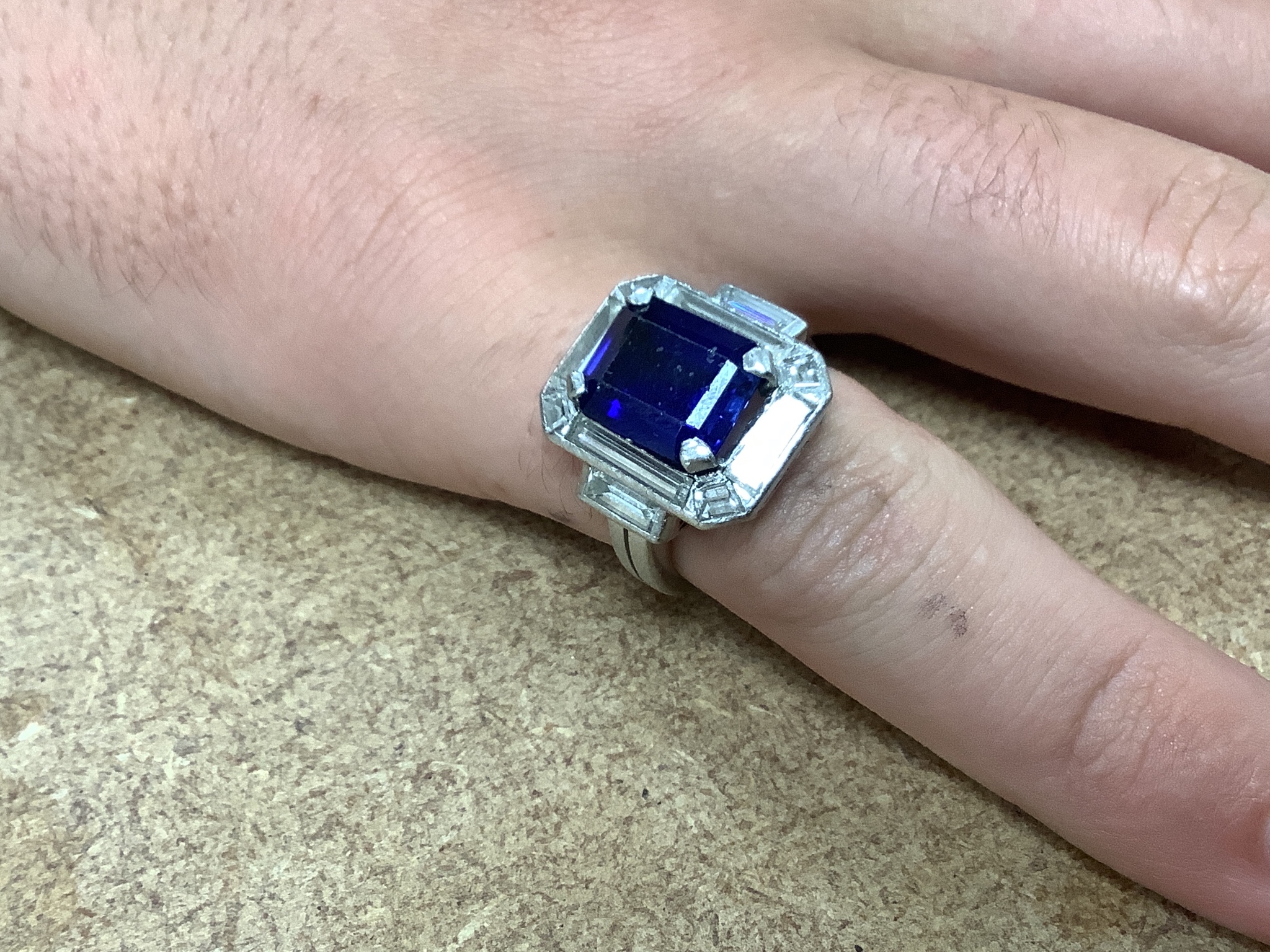 A white metal (stamped plat? synthetic sapphire, baguette and trapeze cut diamond set dress ring, size L, gross weight 11.1 grams